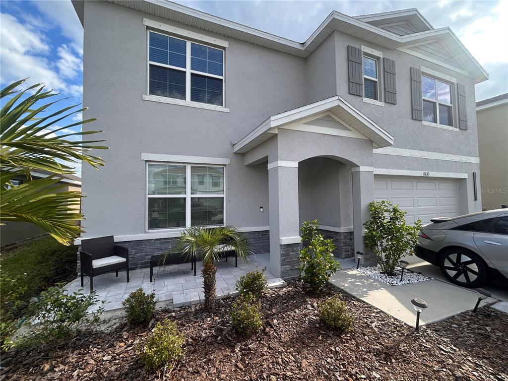 A two-story gray house features a stone-accented base, a covered entryway, and a paved patio — 17630 CANOPY PLACE, BRADENTON, FL