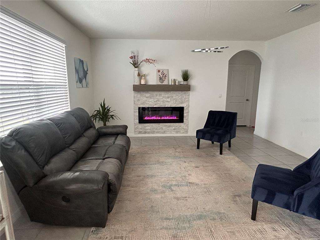 A living room features a grey sofa, two blue chairs, and a stone-faced electric fireplace — 17630 CANOPY PLACE, BRADENTON, FL