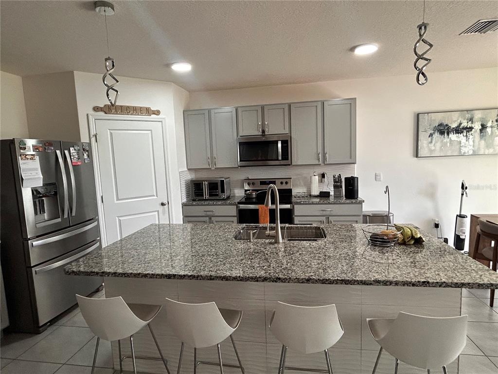 A kitchen features gray cabinets, granite countertops, a large island, and stainless steel appliances — 17630 CANOPY PLACE, BRADENTON, FL