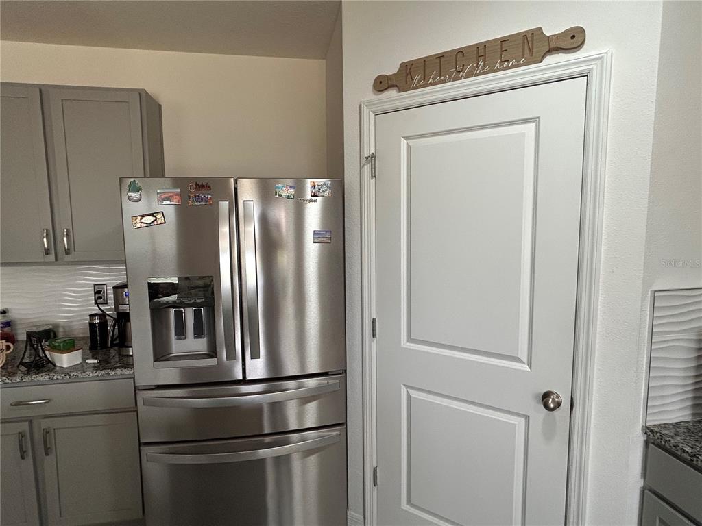 A stainless steel refrigerator stands next to a white door in a kitchen with gray cabinets — 17630 CANOPY PLACE, BRADENTON, FL