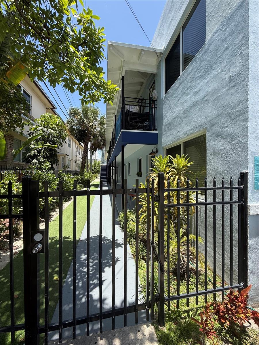 A black metal gate opens to a walkway alongside a two-story blue apartment building — 1450 Lenox Ave # 5, Miami Beach FL 33139, MIAMI BEACH, FL