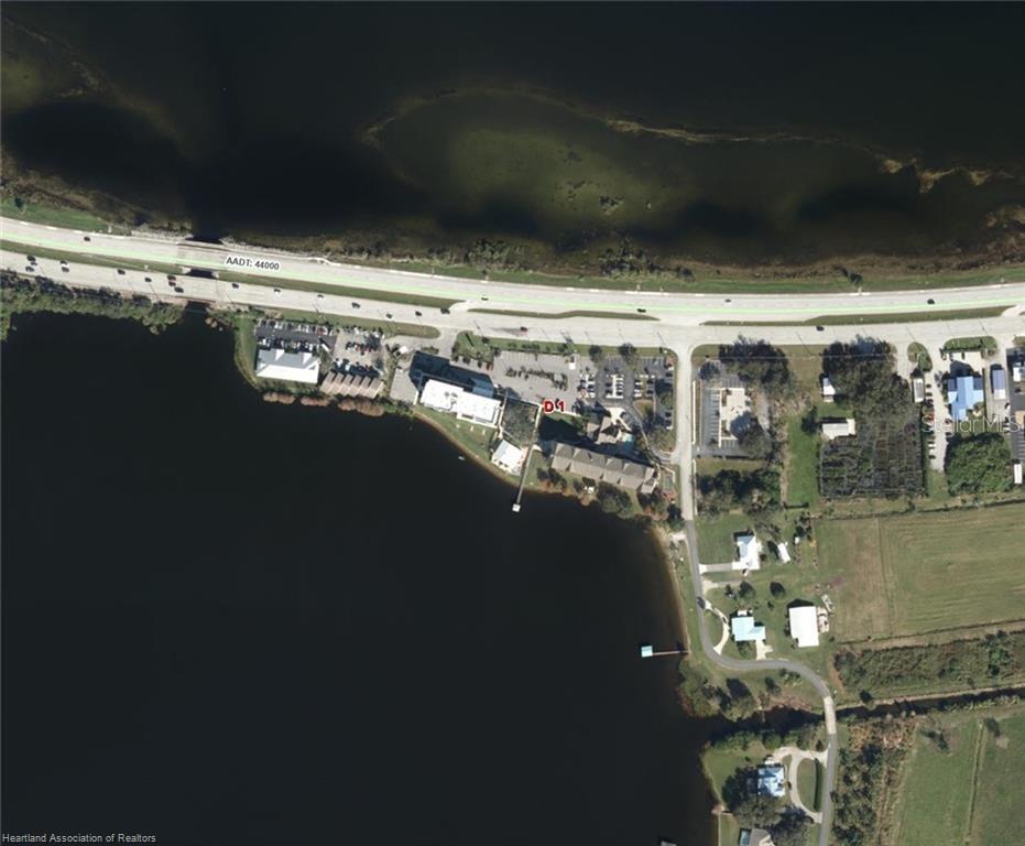 This aerial view shows a waterfront property with a building, parking lot, and nearby road — 1993 US HIGHWAY 27 S, SEBRING, FL