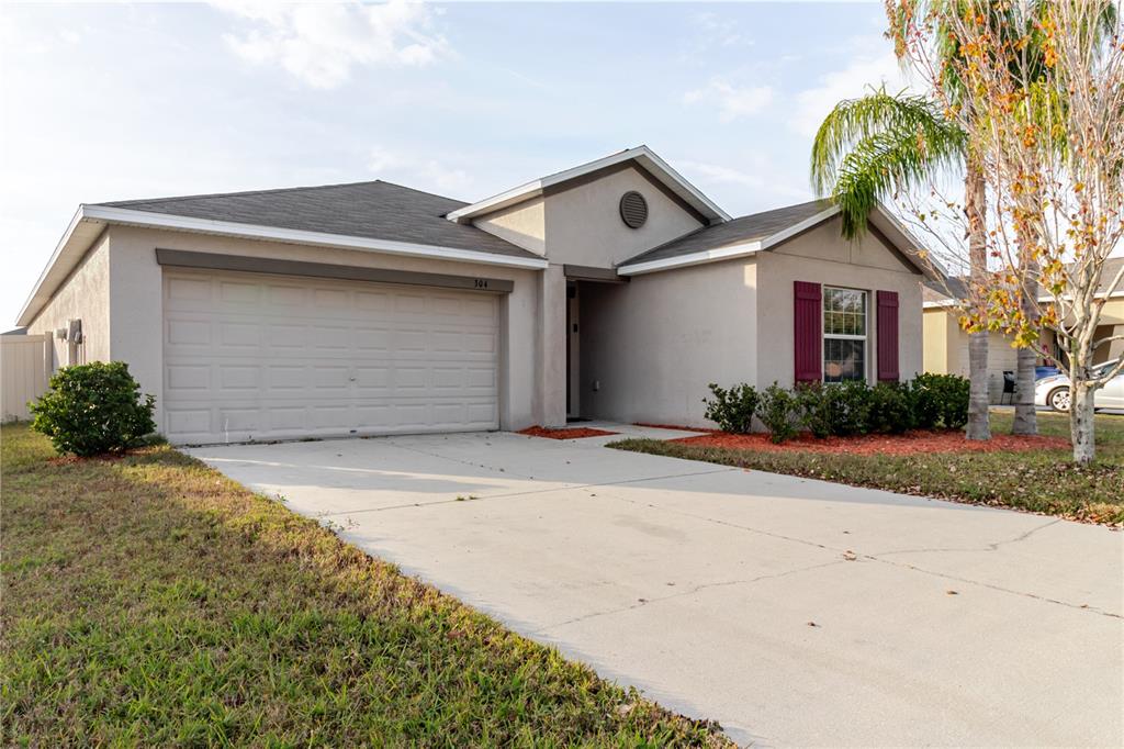 A single-story house with a beige stucco exterior, a two-car garage, and red window shutters — 304 CASCADE BEND, RUSKIN, FL