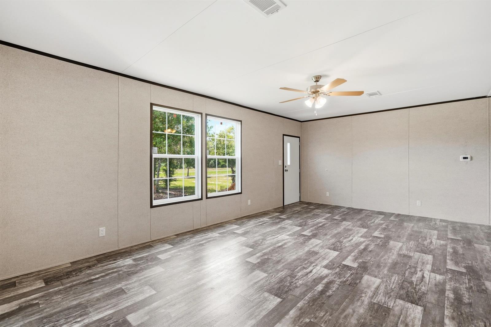 An empty room features light-colored paneled walls, wood-look flooring, two windows, and a ceiling fan — 17381 NW 262nd Street, Okeechobee FL 34972, OKEECHOBEE, FL