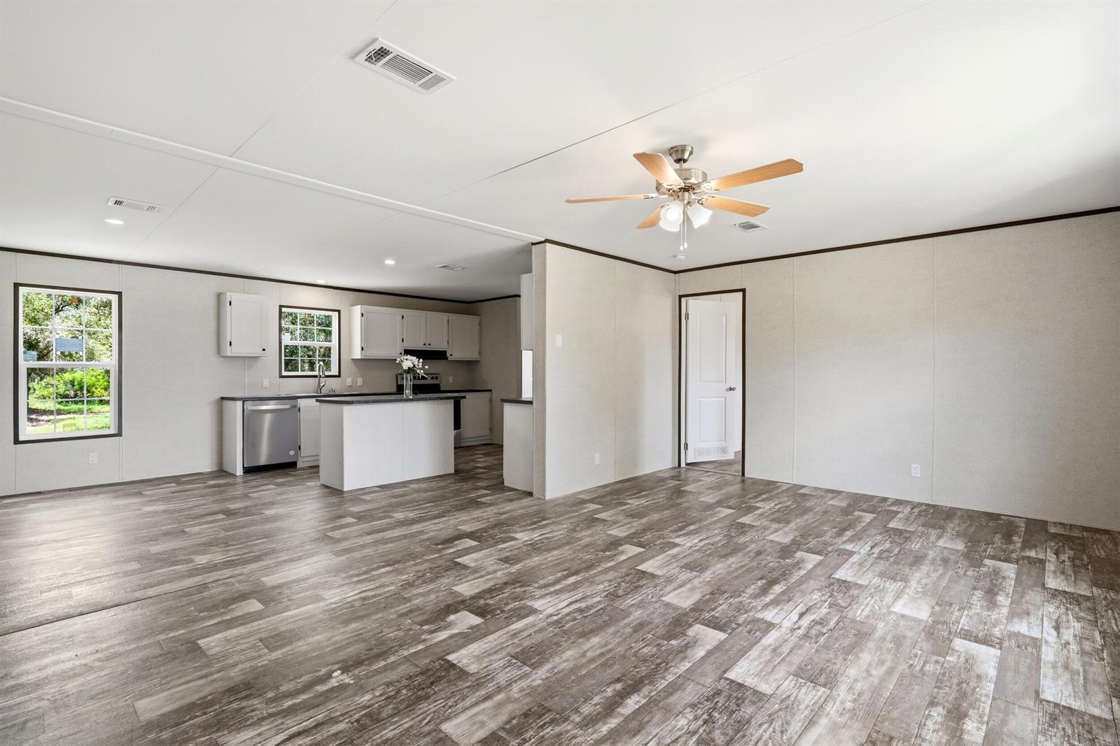 An open-concept living area features wood-look flooring, a ceiling fan, and an adjacent kitchen — 17381 NW 262nd Street, Okeechobee FL 34972, OKEECHOBEE, FL