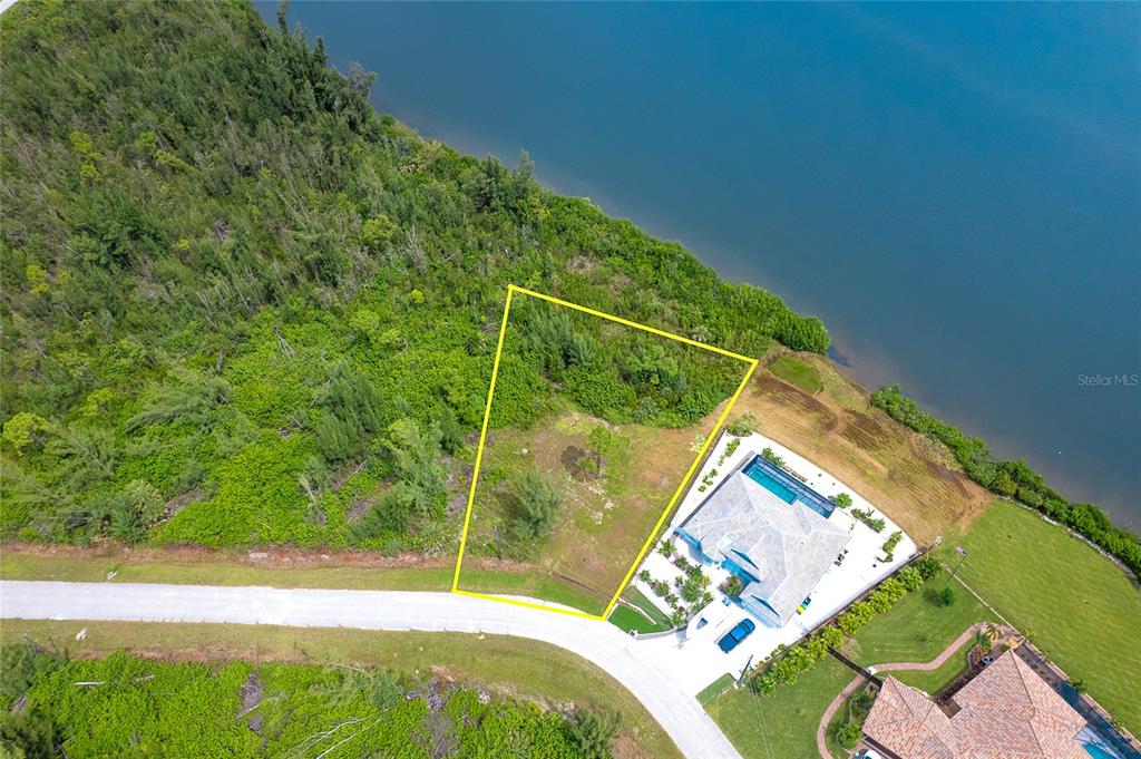 An aerial view shows a vacant, trapezoidal waterfront lot outlined in yellow next to a house — 16468 LIGGETT CIRCLE, PORT CHARLOTTE, FL