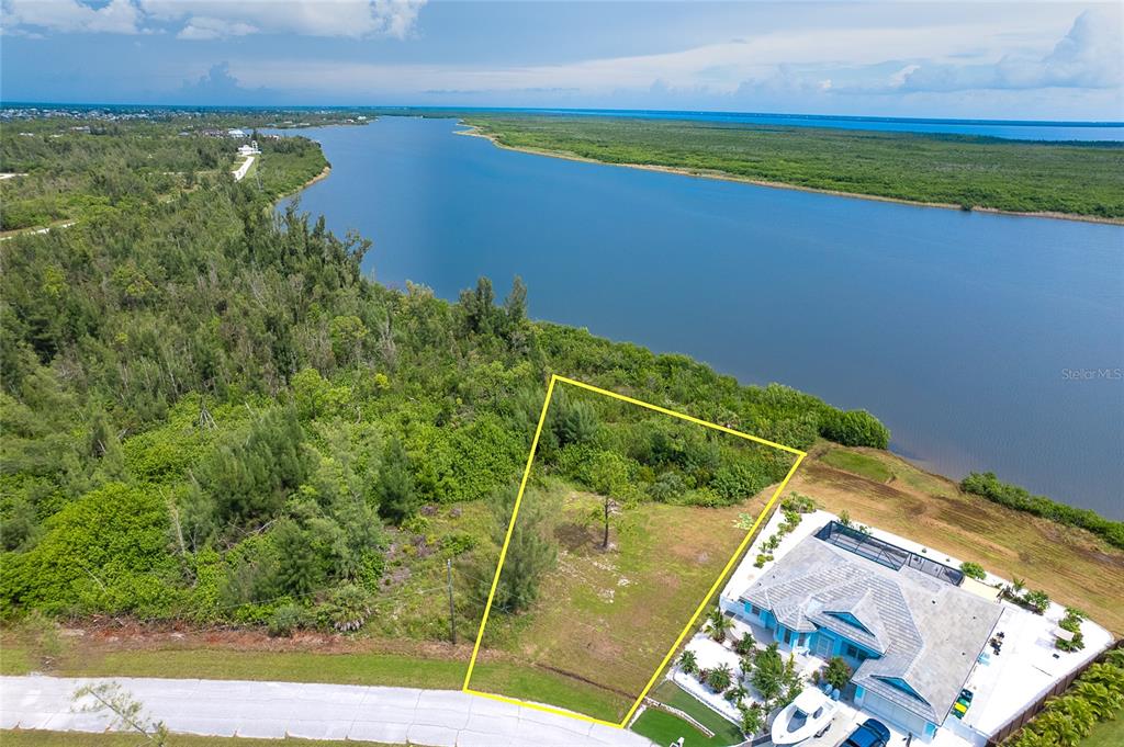 An aerial view shows a vacant waterfront lot outlined in yellow next to a house — 16468 LIGGETT CIRCLE, PORT CHARLOTTE, FL