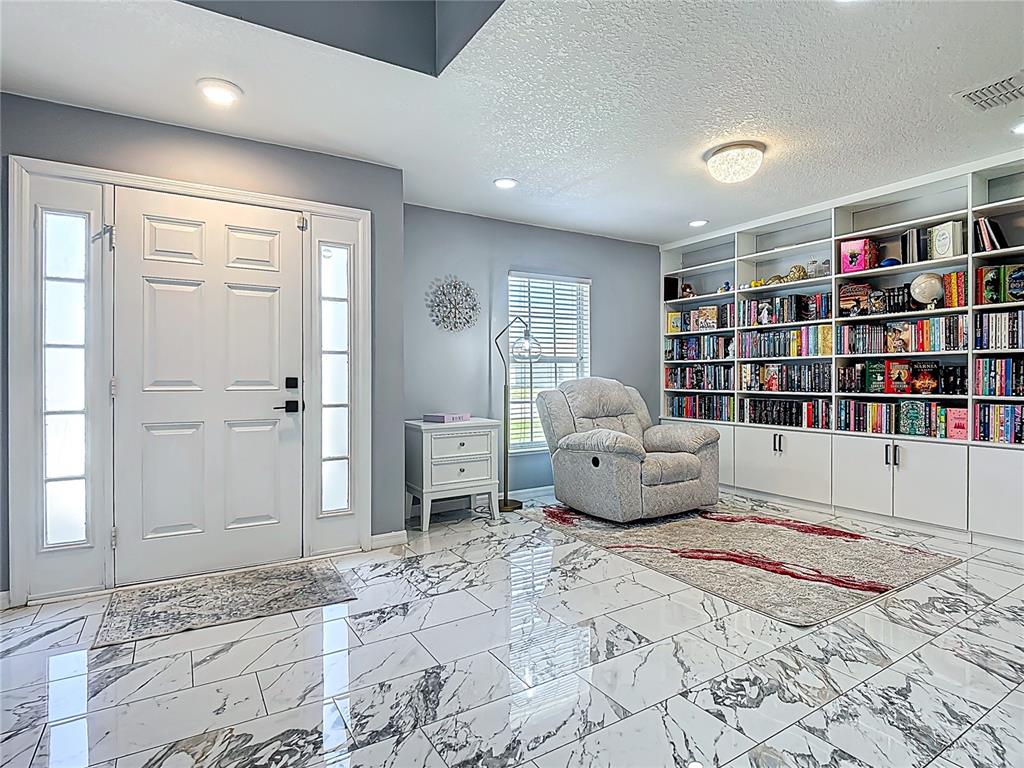 A room with marble-look tile floors, a white front door, and a large built-in bookshelf — 965 ALSACE DRIVE, KISSIMMEE, FL