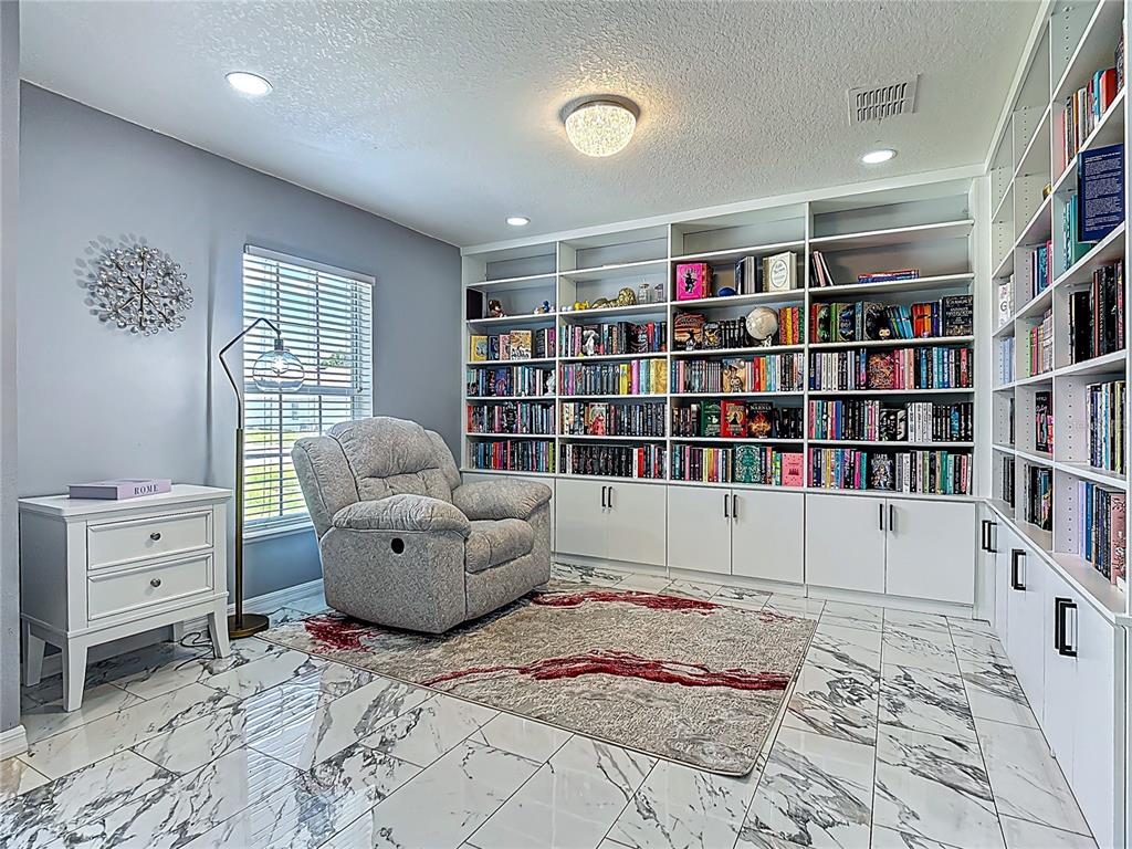 A home library features built-in white bookshelves, a gray recliner, and marble-patterned tile flooring — 965 ALSACE DRIVE, KISSIMMEE, FL