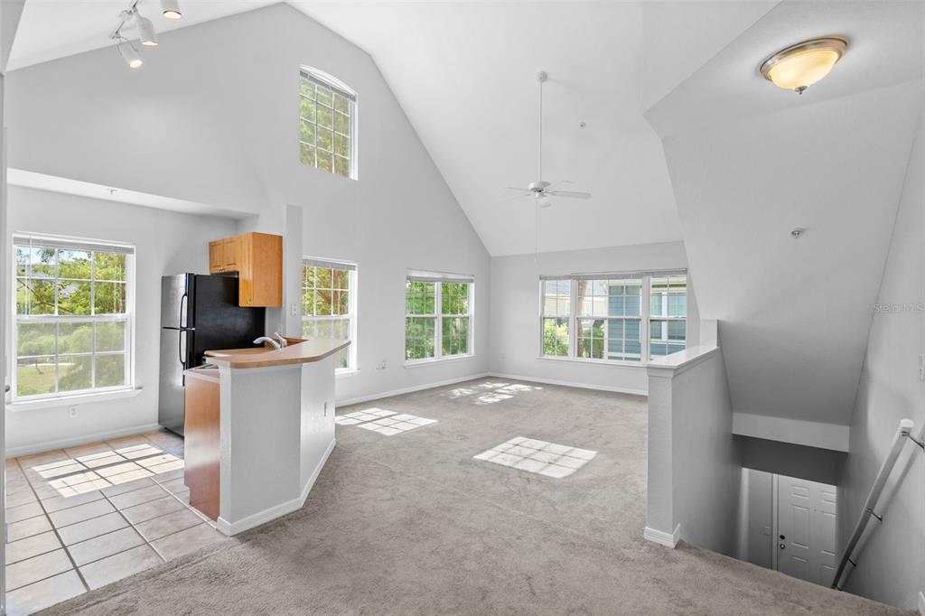 An open-concept living area features vaulted ceilings, carpeted flooring, and an adjacent kitchen with tile — 5611 BIDWELL PARKWAY UNIT 204, SARASOTA, FL