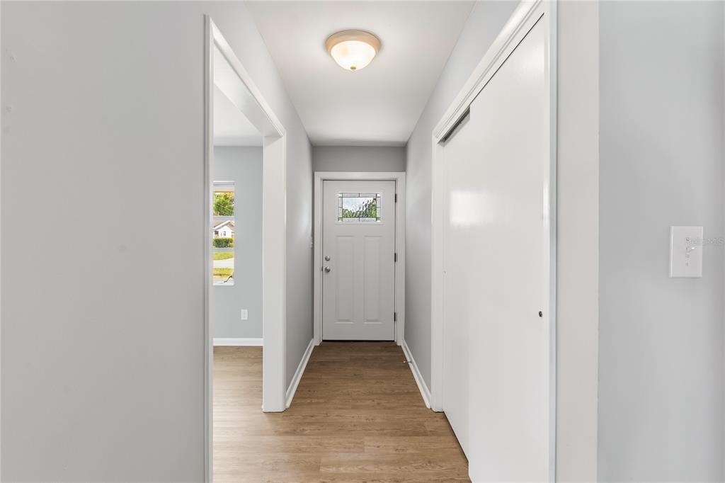 A hallway with light wood-look flooring leads to a white front door with a window — 6 GOLFVIEW CIRCLE NE, WINTER HAVEN, FL
