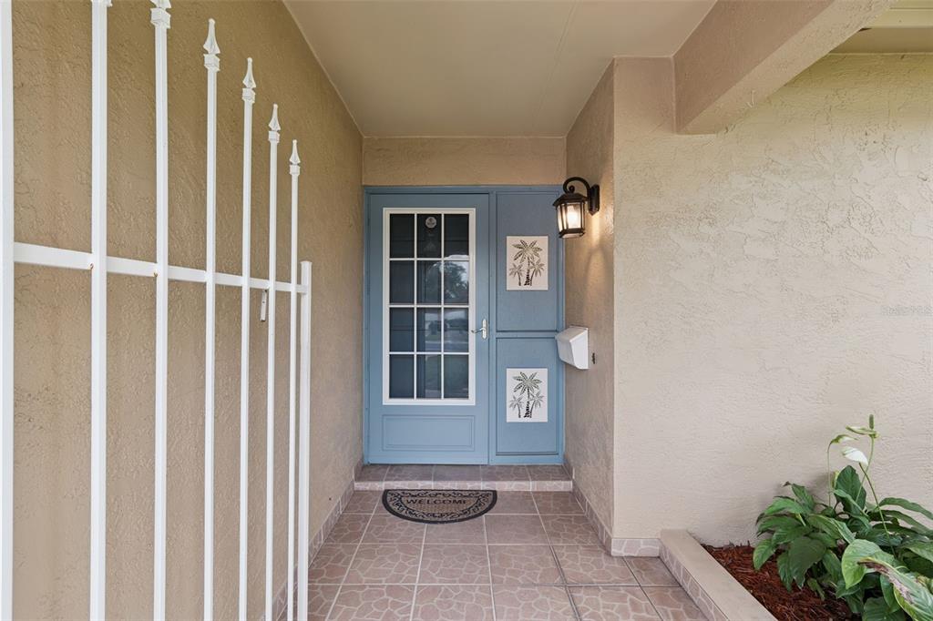 A blue front door with a glass panel and palm tree accents sits under a porch — 1391 AVALON BOULEVARD, CASSELBERRY, FL