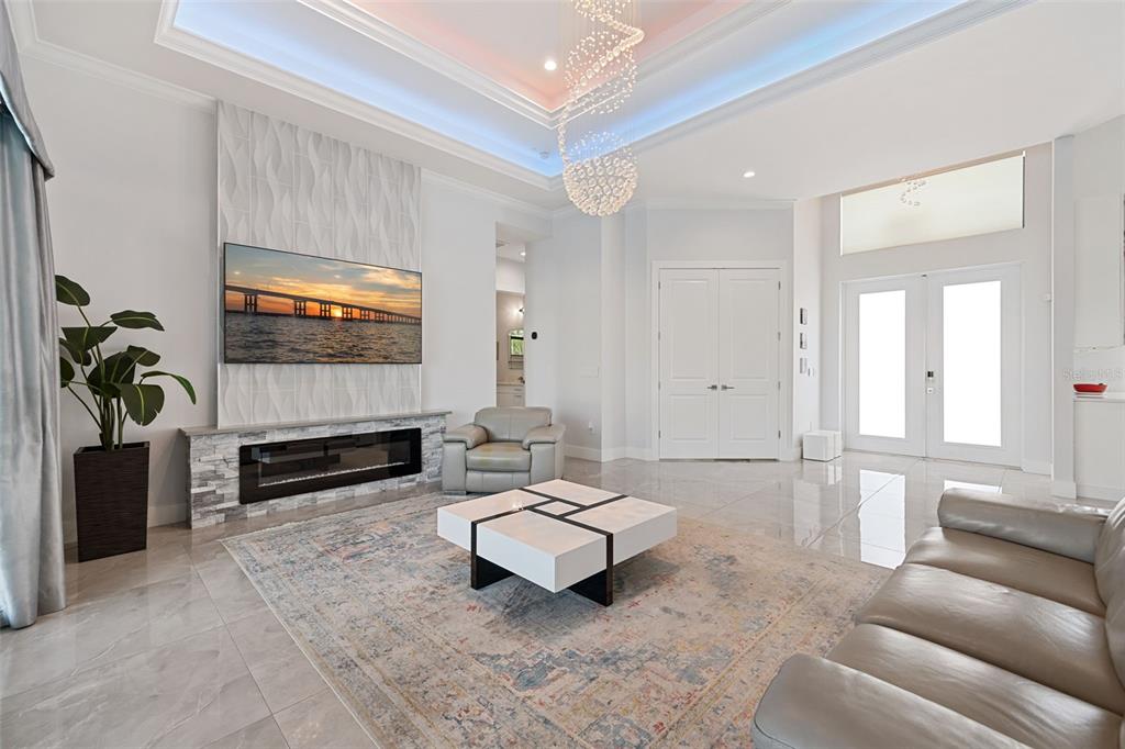 A modern living room features a fireplace, a large television, and a crystal chandelier — 3619 SE 16TH PLACE, CAPE CORAL, FL