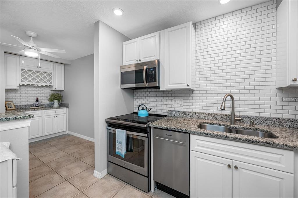 A kitchen features white cabinets, granite countertops, stainless steel appliances, and a white subway tile backsplash — 3295 FOX CHASE UNIT 105, PALM HARBOR, FL