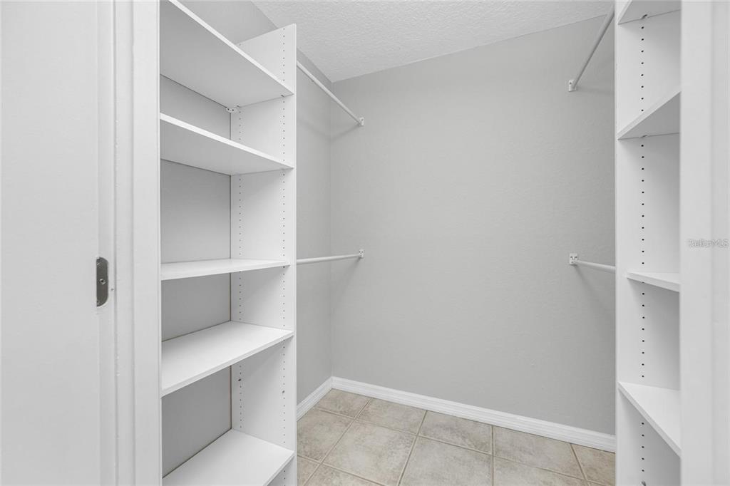 A walk-in closet features white shelving units, hanging rods, and light-colored tile flooring — 3295 FOX CHASE UNIT 105, PALM HARBOR, FL