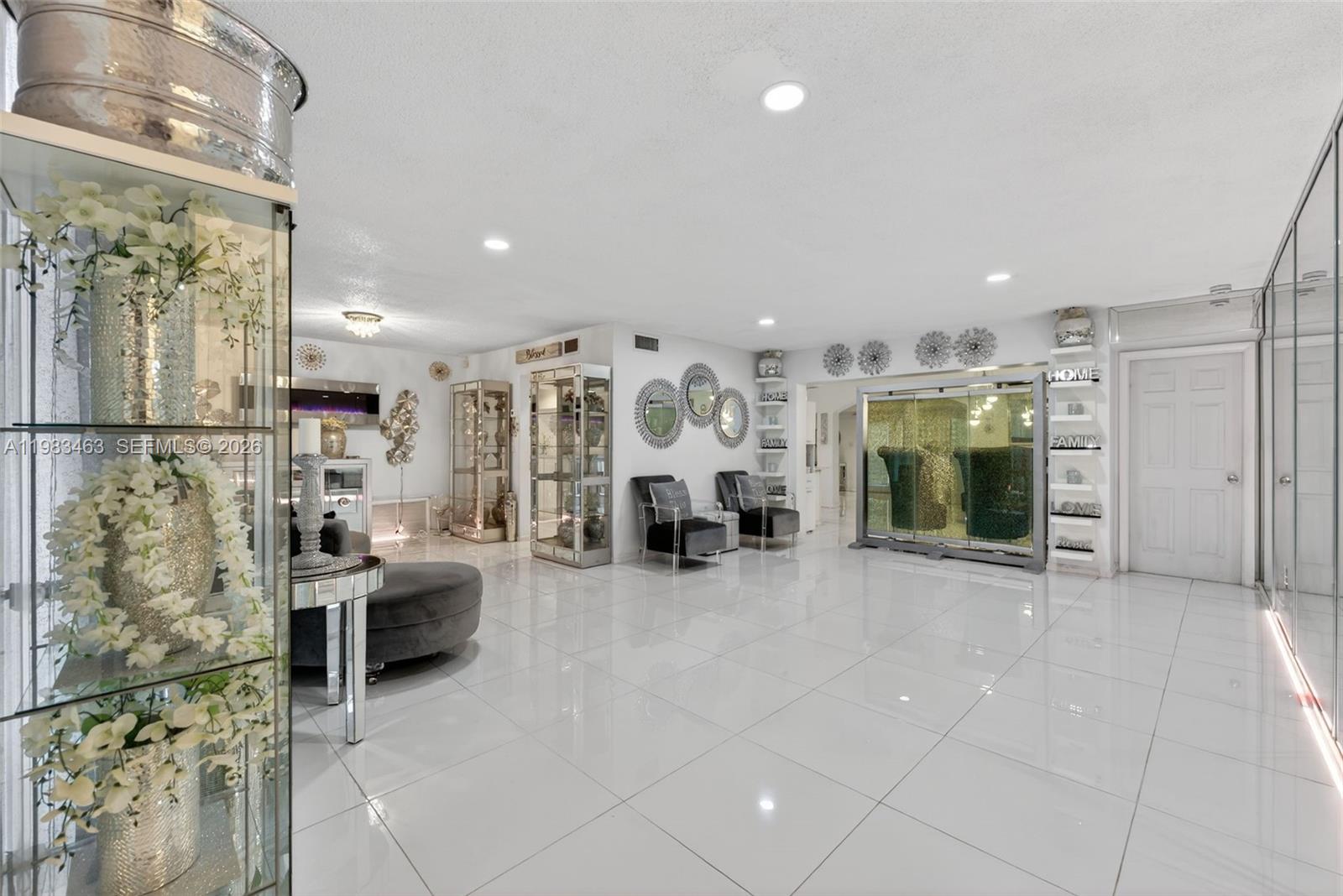 A bright, open-concept living area features white tile flooring, mirrored display cabinets, and modern decor — 7777 Fairway Blvd, Miramar FL 33023, MIRAMAR, FL