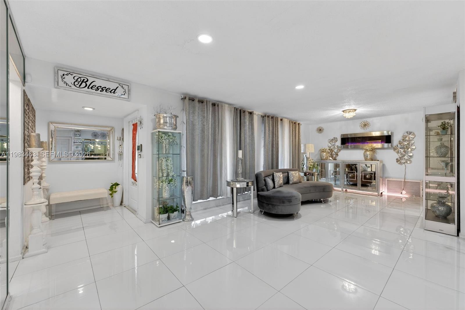 A bright living room features white tile floors, a grey curved sofa, and a fireplace — 7777 Fairway Blvd, Miramar FL 33023, MIRAMAR, FL