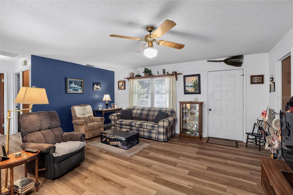 A living room features a blue accent wall, plaid sofa, brown recliner, and wood-look flooring — 2651 SAMPLE STREET, KISSIMMEE, FL