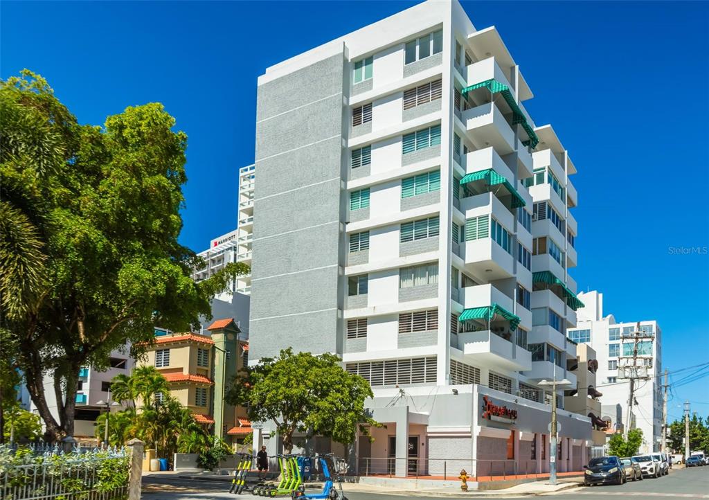 A multi-story white apartment building with green balcony awnings stands on a sunny street corner — 1319 ASHFORD UNIT PH, SAN JUAN, PR