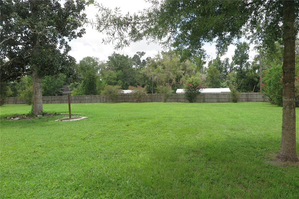 A large, grassy backyard features mature trees and a wooden fence along the back perimeter — 105 SE 1ST AVENUE, LAKE BUTLER, FL