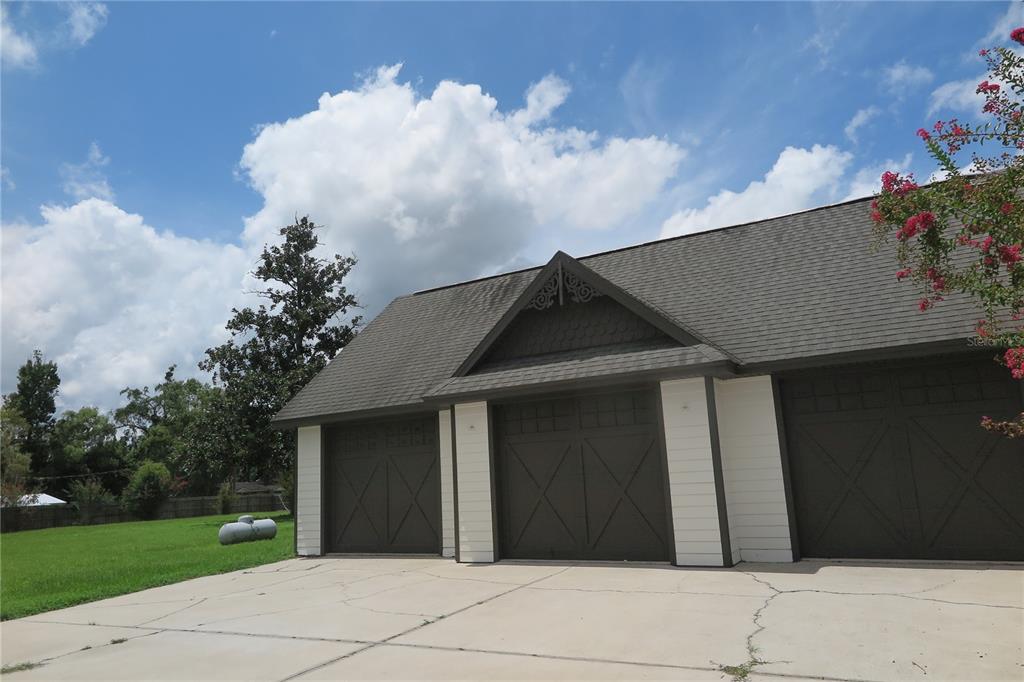 A detached three-car garage with dark brown doors and a gabled roof under a blue sky — 105 SE 1ST AVENUE, LAKE BUTLER, FL