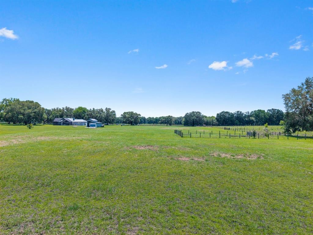 A large, grassy field features a distant house and a fenced area under a sky — TBD NW 56TH LANE, NEWBERRY, FL