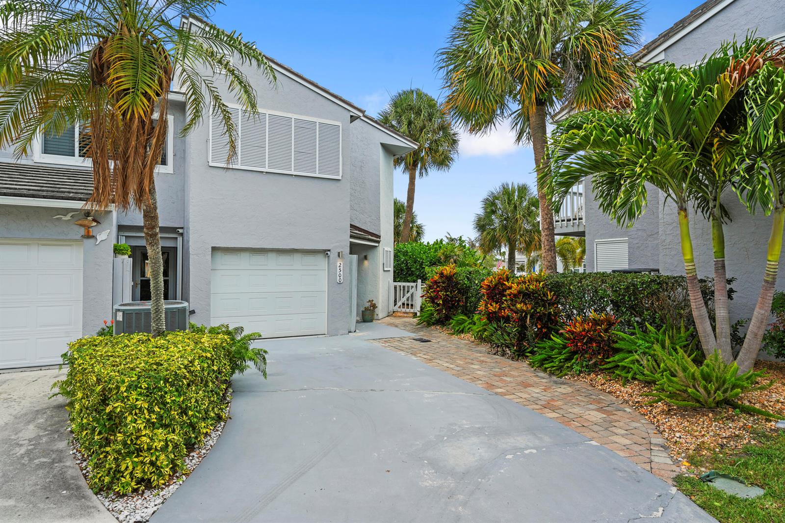 A gray two-story townhouse with a concrete driveway, a garage, and tropical landscaping — FORT PIERCE, FL