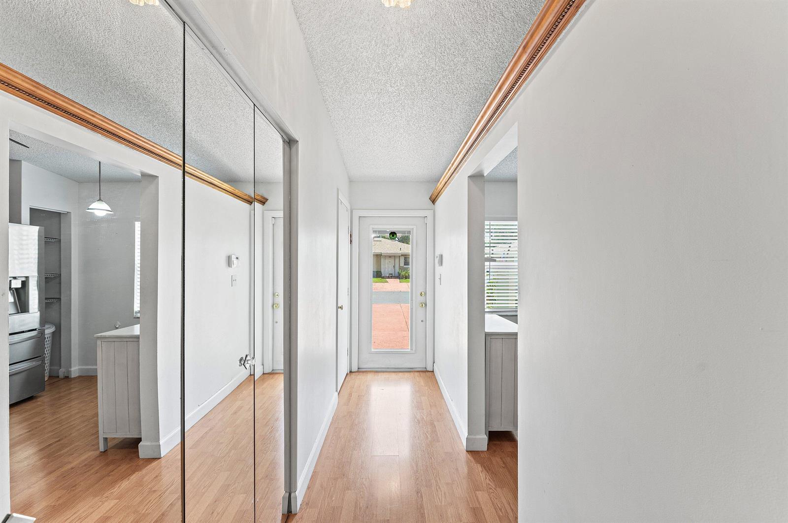 A hallway with wood-look flooring, mirrored closet doors, and a glass-paneled front door — 18855 Candlewick Drive, Boca Raton FL 33496, BOCA RATON, FL