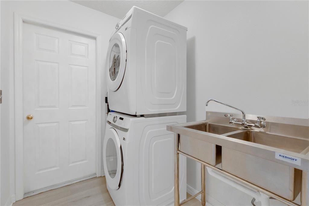 A laundry room features a stacked washer and dryer next to a stainless steel sink — 558 PINNACLE DRIVE, HAINES CITY, FL