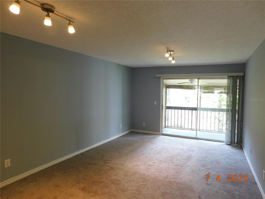 An empty living room features gray walls, carpeted flooring, track lighting, and a sliding glass door — 6314 NEWTOWN CIRCLE UNIT 14B3, TAMPA, FL