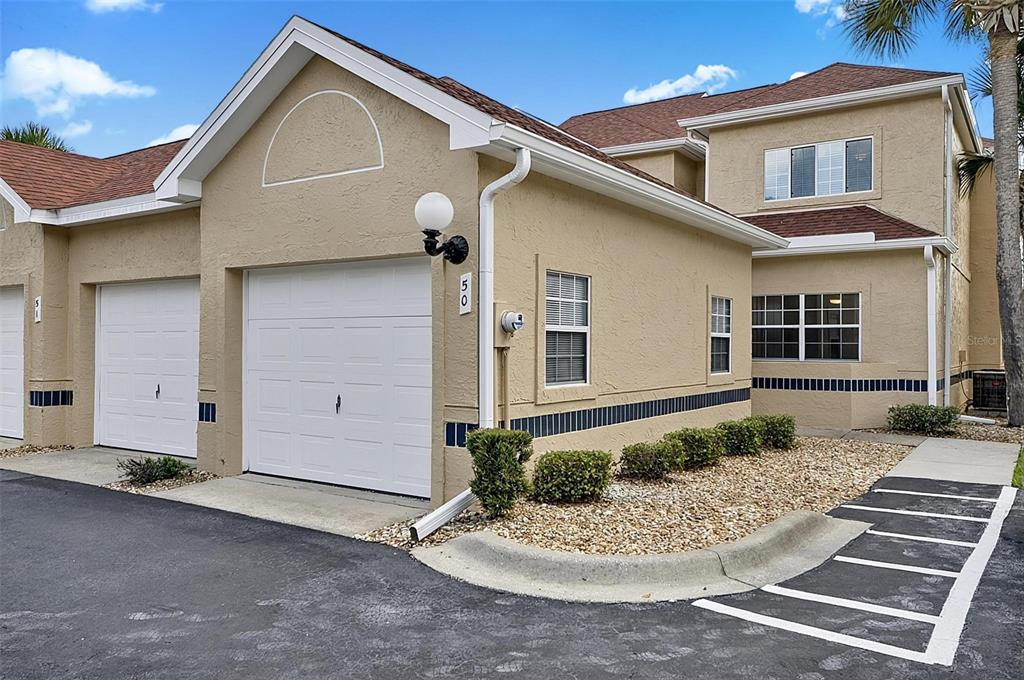 A tan two-story townhouse with a white garage door and a small gravel garden — 50 RIVERS EDGE LANE, PALM COAST, FL