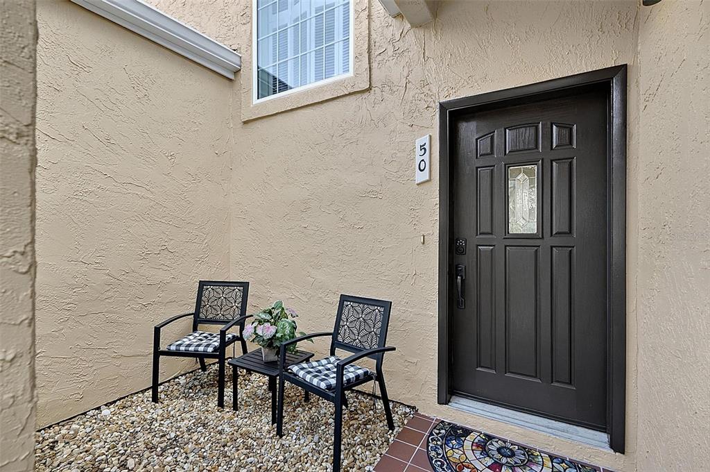 A small gravel patio with two chairs and a table sits beside a dark front door — 50 RIVERS EDGE LANE, PALM COAST, FL