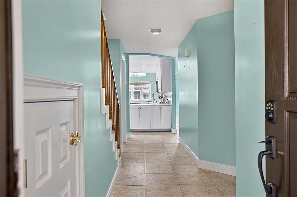 A hallway with light blue walls, tile flooring, and a staircase leads to a kitchen — 50 RIVERS EDGE LANE, PALM COAST, FL