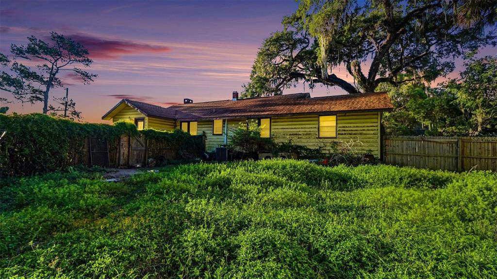The exterior of a single-story house with yellow siding sits behind a large, grassy yard — 833 NE 28TH STREET, OCALA, FL