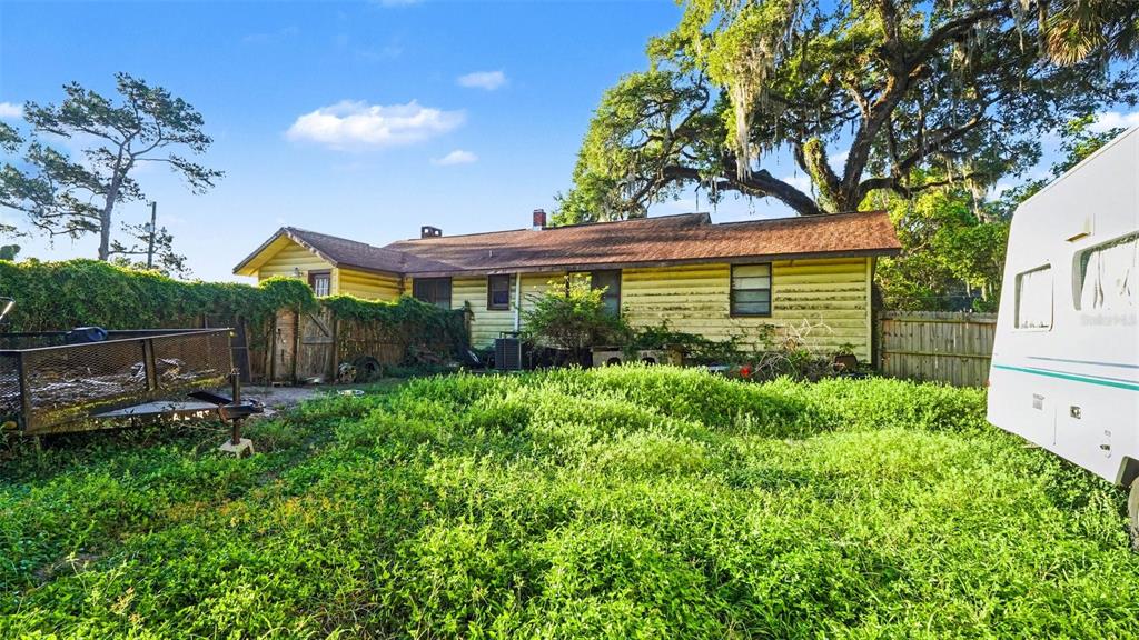 The exterior of a yellow house with a brown roof sits behind an overgrown yard — 833 NE 28TH STREET, OCALA, FL