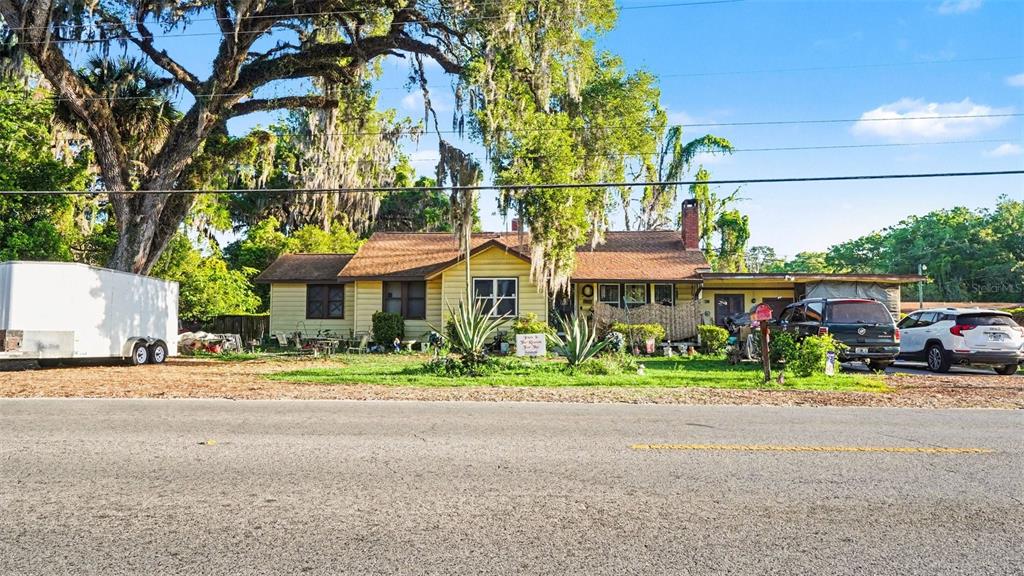 A yellow single-story house with a brown roof sits behind a road and large trees — 833 NE 28TH STREET, OCALA, FL