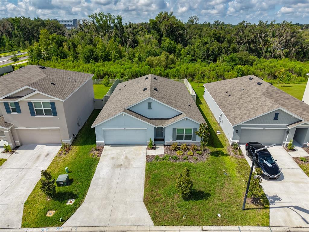 An aerial view shows three suburban houses with driveways and lawns bordering a wooded area — 1902 TAHITIAN SUNRISE DRIVE, PLANT CITY, FL