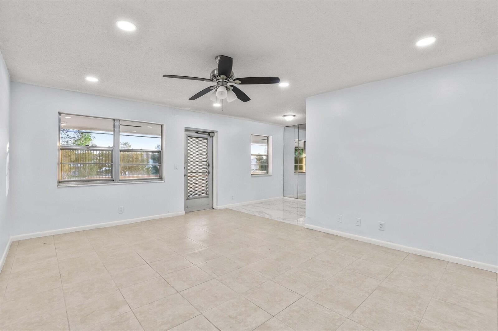 A bright, tiled living room features a ceiling fan, recessed lighting, and a glass-paned door — 63 Hastings D, West Palm Beach FL 33417, WEST PALM BEACH, FL