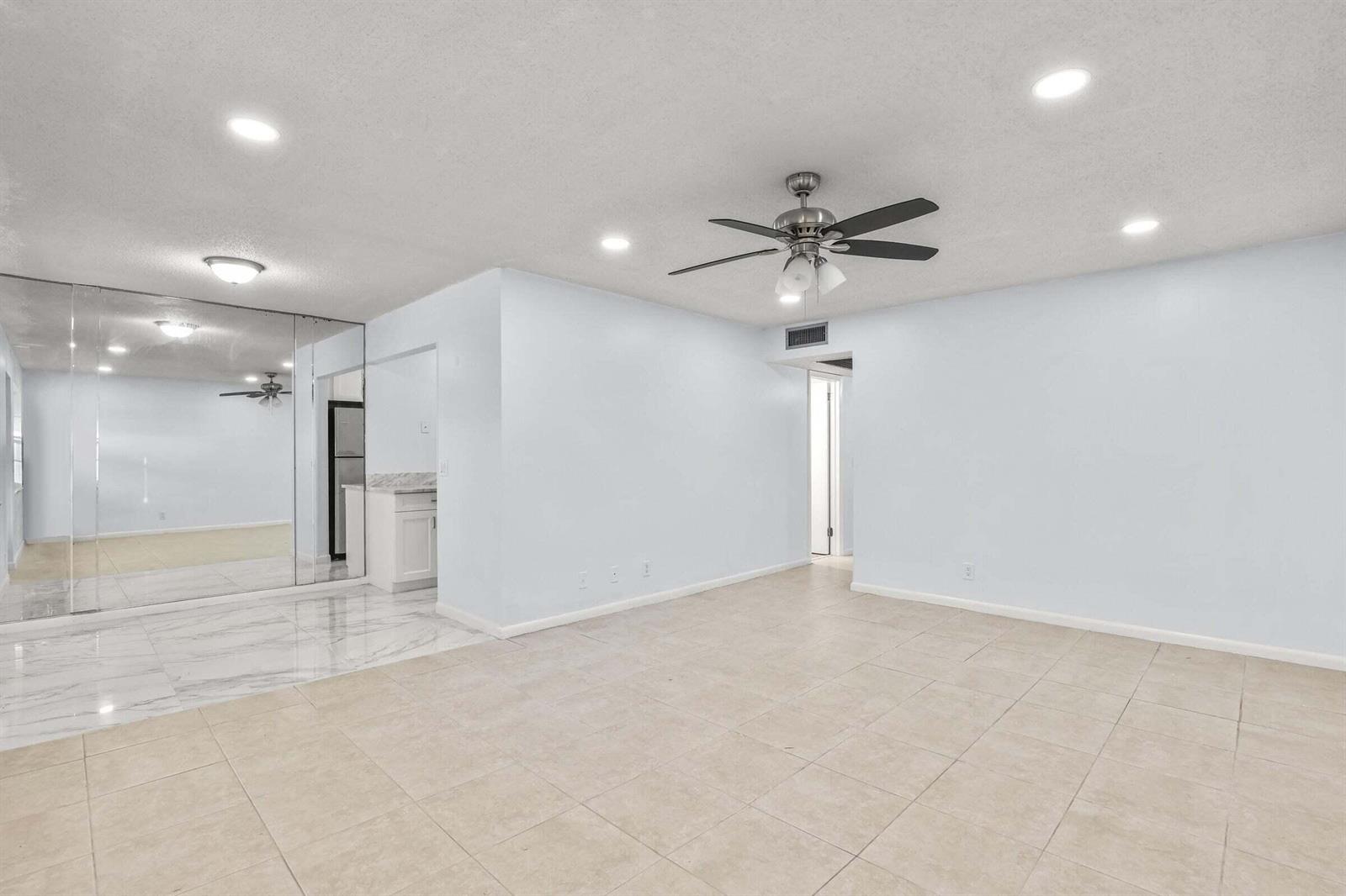 A bright, open living room features light-colored tile flooring, a ceiling fan, and mirrored walls — 63 Hastings D, West Palm Beach FL 33417, WEST PALM BEACH, FL
