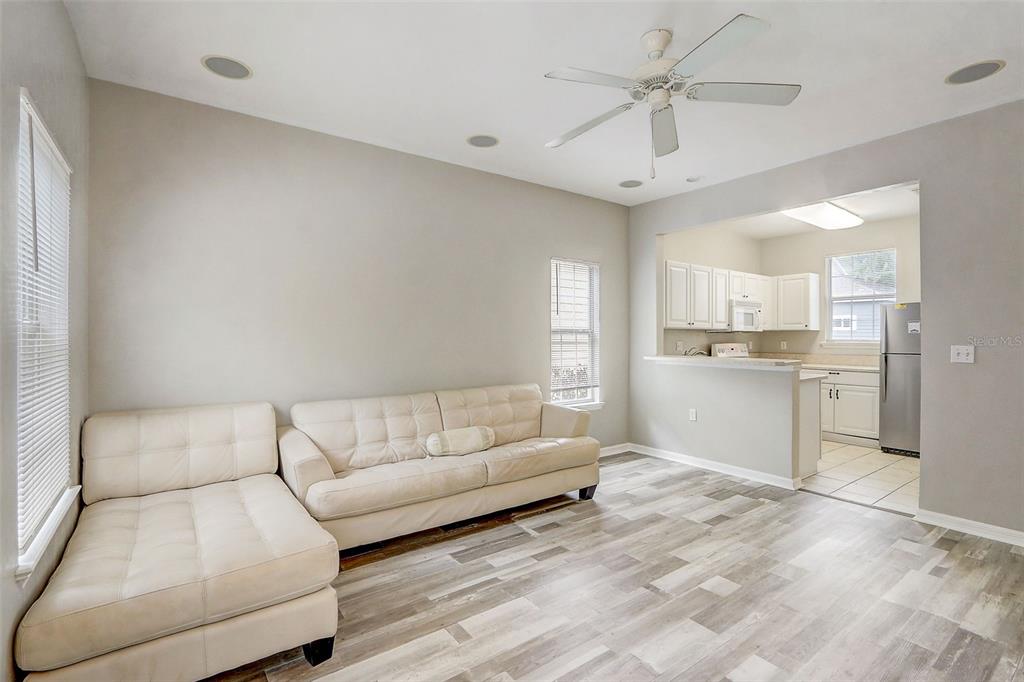 A living room with a white sectional sofa, wood-look flooring, and an open kitchen — 5116 NW 21ST DRIVE, GAINESVILLE, FL