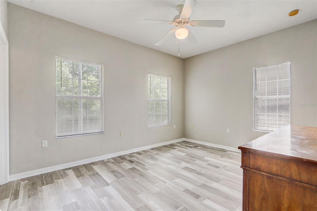 An empty bedroom features light gray walls, wood-look flooring, three windows, and a ceiling fan — 5116 NW 21ST DRIVE, GAINESVILLE, FL