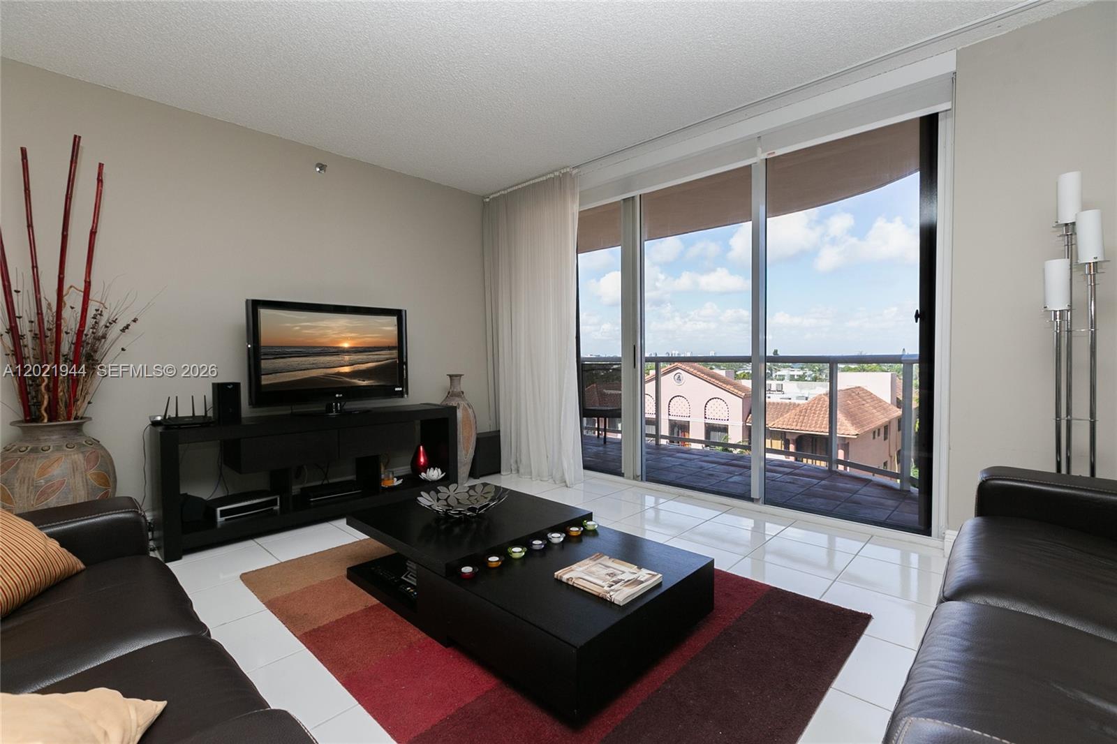 An elevated view from a balcony overlooking a street, palm trees, and city buildings at dusk — 8855 Collins Ave # 6F, Surfside FL 33154, SURFSIDE, FL
