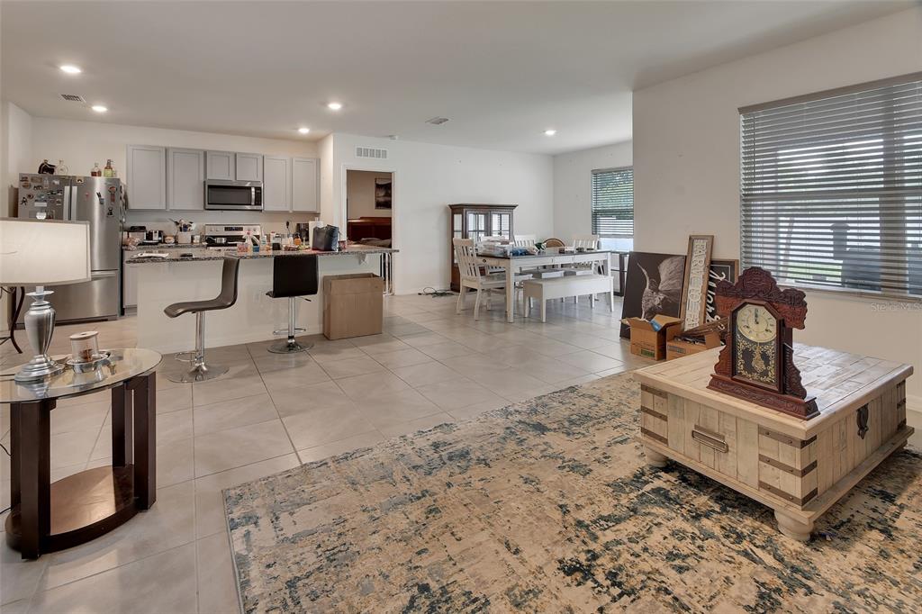 An open-concept kitchen and living area features light tile flooring, gray cabinetry, and a rug — 1235 WINTER GRAY CIRCLE, DELTONA, FL