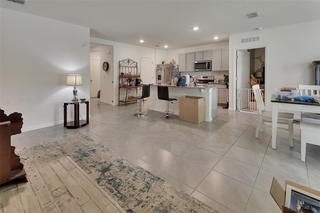 An open-concept kitchen and living area features light tile flooring, white cabinetry, and a breakfast bar — 1235 WINTER GRAY CIRCLE, DELTONA, FL