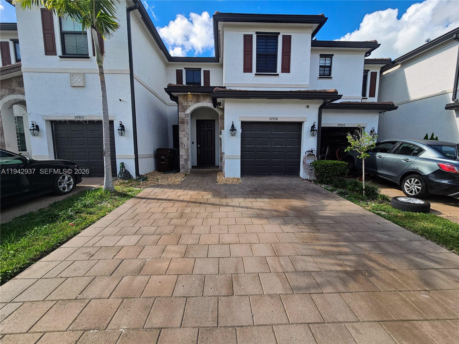 A two-story residential building features a paved driveway, dark garage doors, and white stucco walls — 10918 W 33rd Way, Hialeah FL 33018, HIALEAH, FL