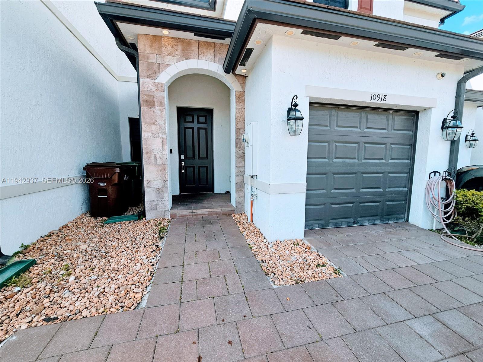 The exterior of a house features a dark front door, garage, and stone-paved walkway — 10918 W 33rd Way, Hialeah FL 33018, HIALEAH, FL