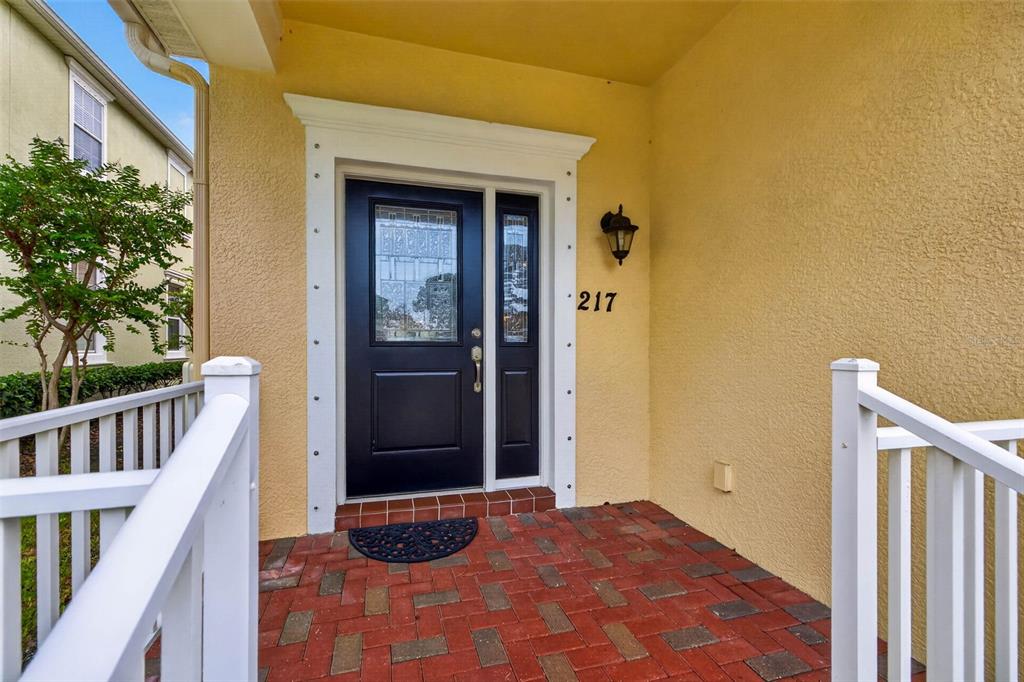 A front porch with a brick floor, white railings, and a dark door with sidelights — 217 49TH AVENUE N, ST PETERSBURG, FL