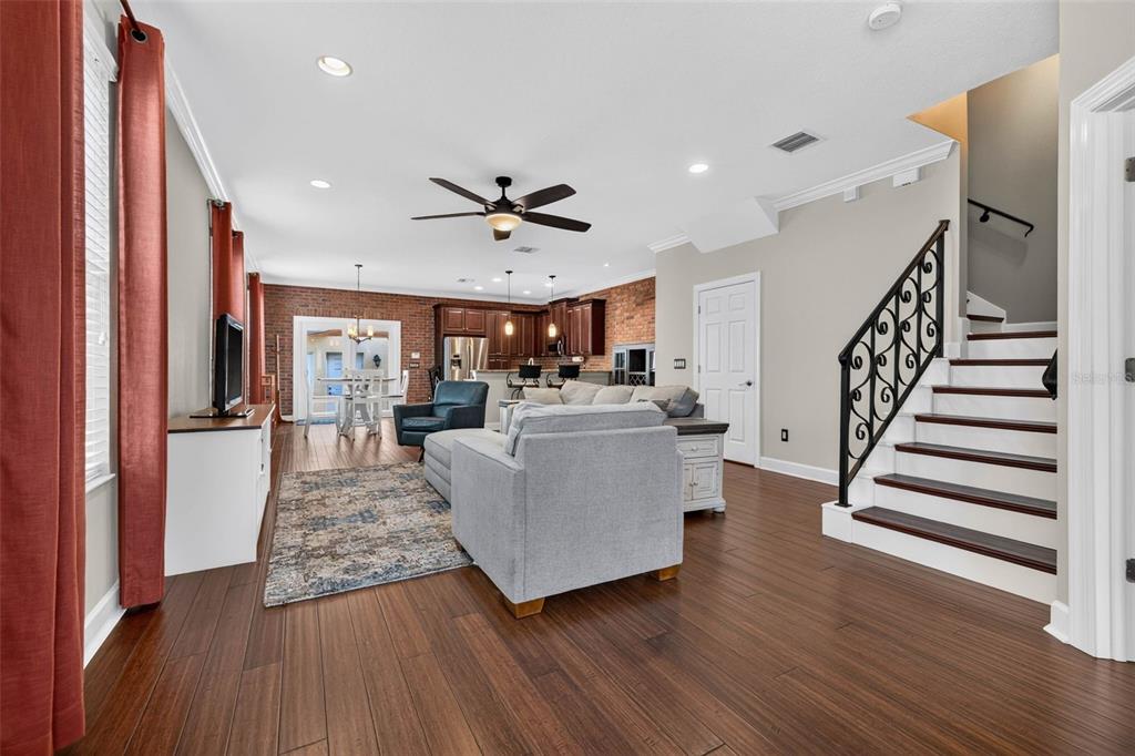 An open-concept living room features hardwood floors, a brick accent wall, and a staircase — 217 49TH AVENUE N, ST PETERSBURG, FL