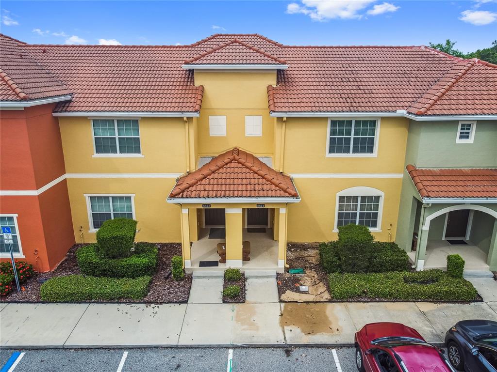 An exterior view of a two-story yellow townhouse with a tiled roof and entryway — 8841 CANDY PALM ROAD, KISSIMMEE, FL