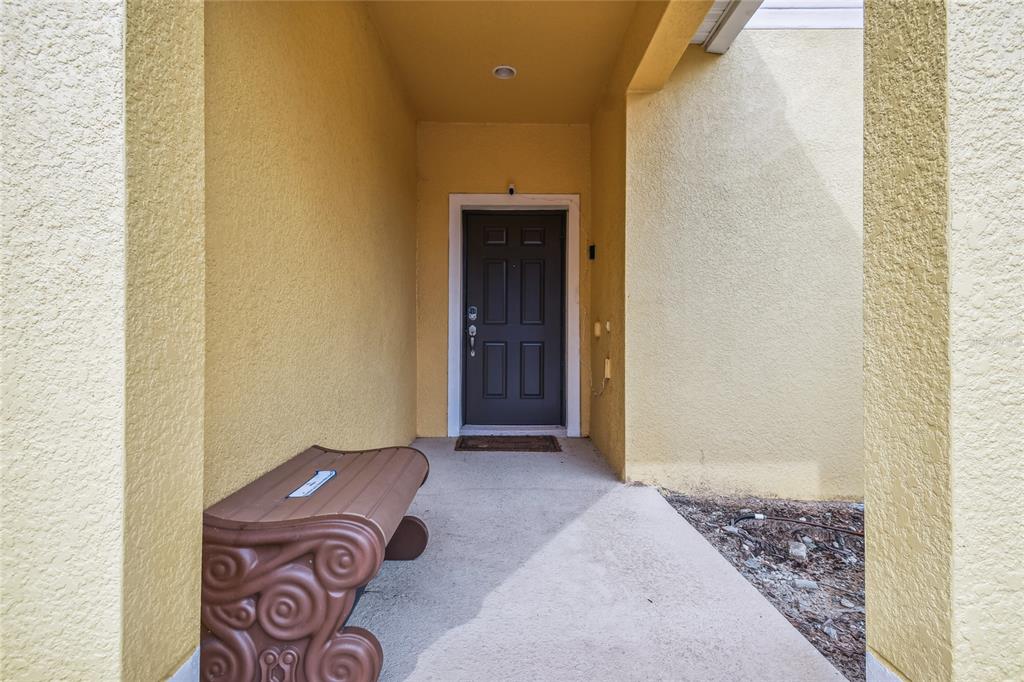 A brown bench sits on a concrete porch in front of a dark entry door — 8841 CANDY PALM ROAD, KISSIMMEE, FL